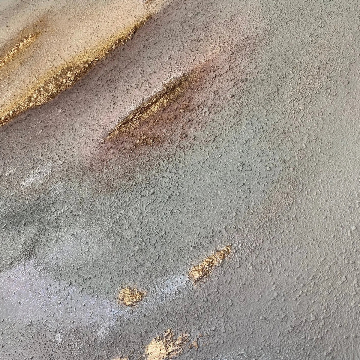 A close-up of a textured gray mixed-media painting with patches of gold.
